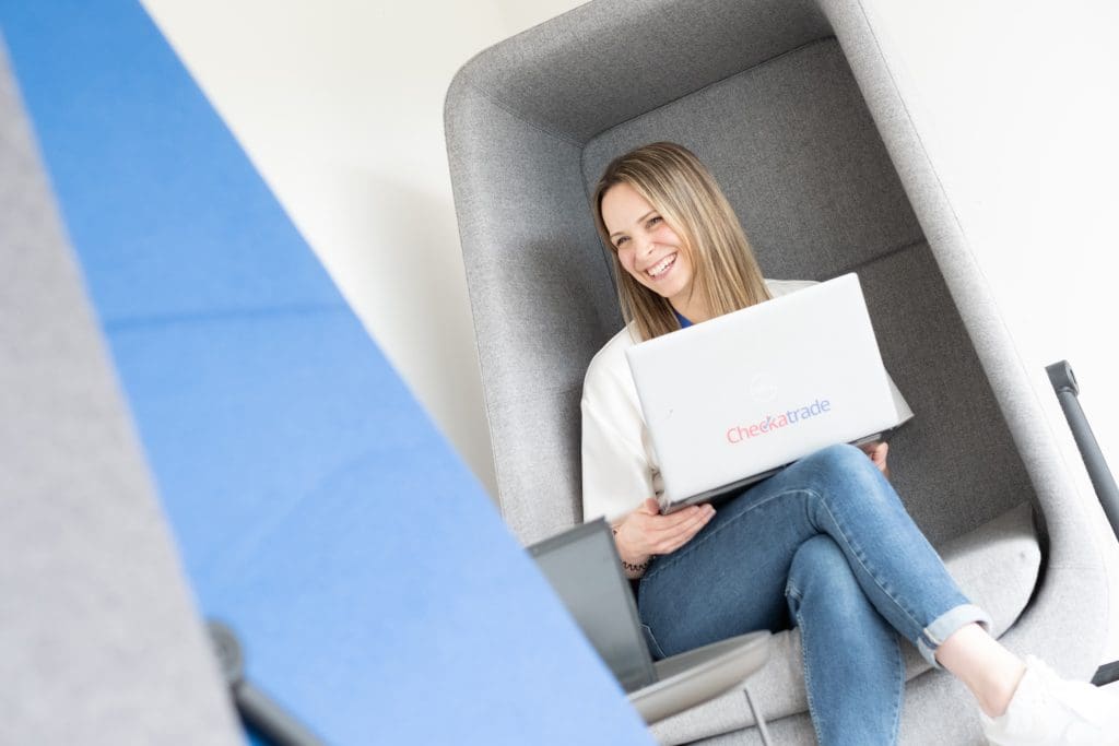 women smiling with legs folder in grey egg chair with laptop on lap