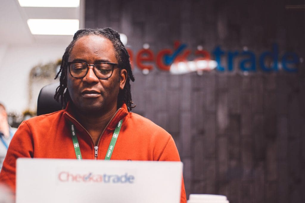 man with glasses and platted hair in orange jacket working at laptop,