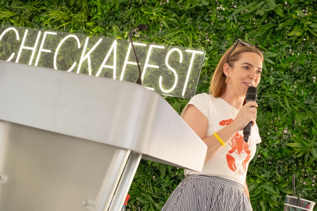 woman with microphone and green flower wall behind her