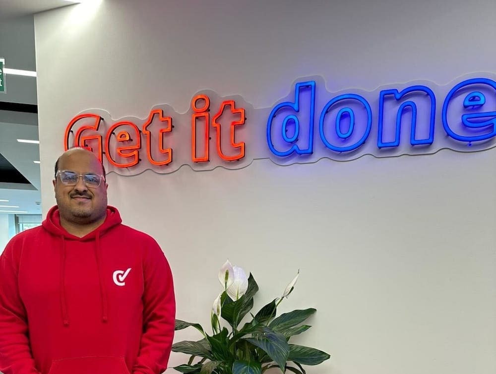 Man wearing red checkatrade hoopie in front of 'Get It Done' neon sign